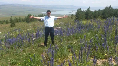 Çıldır’da çiçekli bir yaylada kollarını açmış bir adam, arkada göl