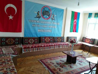 Kilimlerle döşenmiş dernek salonu, duvarda bayraklar ve dernek pankartı